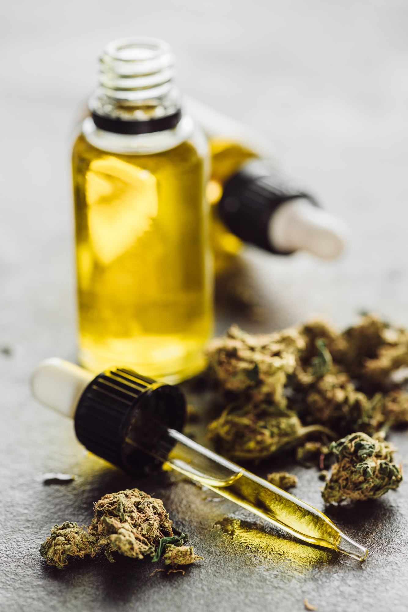 Selective Focus of Dropper With Hemp Oil, Medical Marijuana Buds And Bottles on Stone Surface